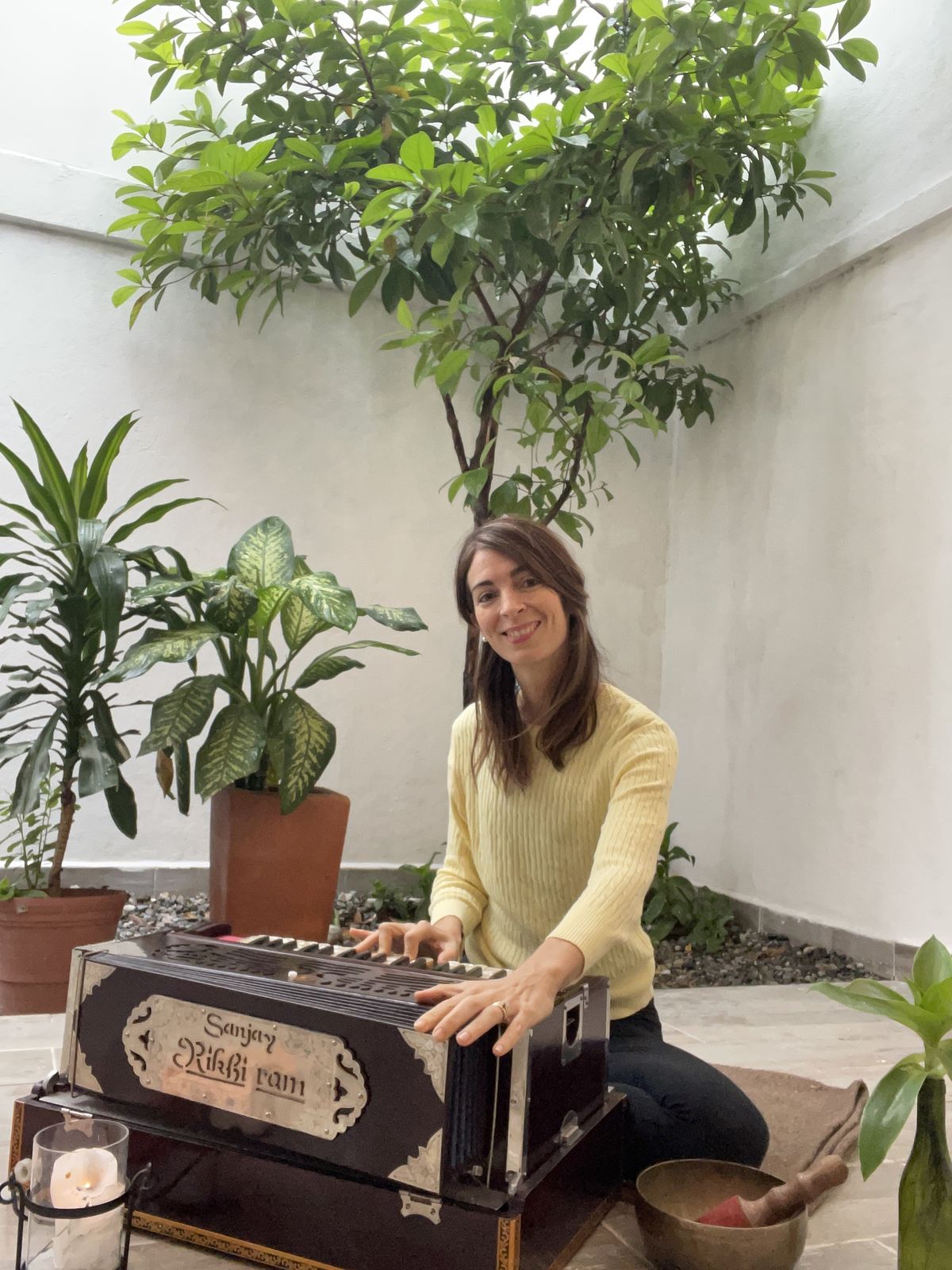Ceci Molina tocando el armonio en el patio de Centro Florecer, con un árbol, plantas, una vela y un cuenco