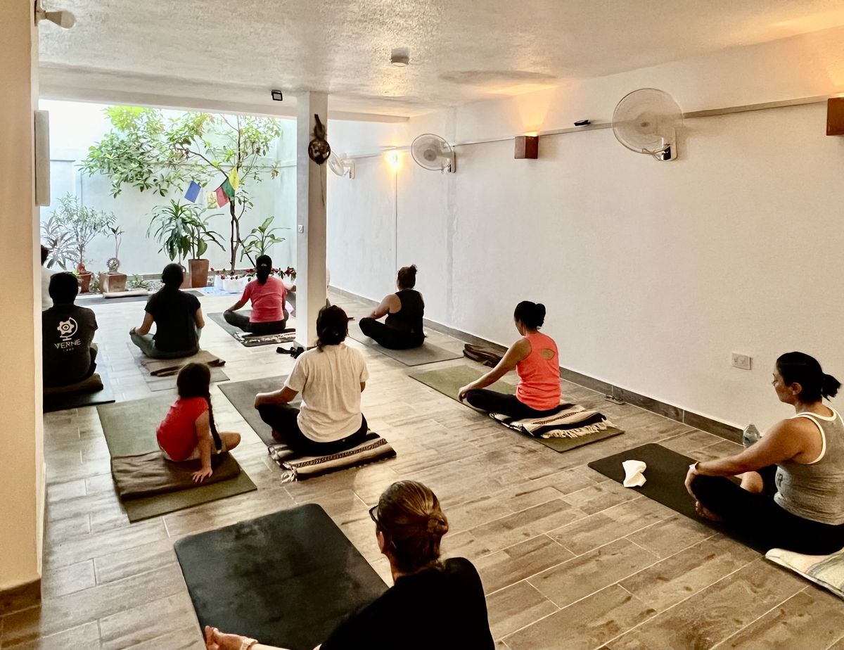Grupo sentado meditando en el salón de Centro Florecer, con el patio y las banderas de oración al fondo
