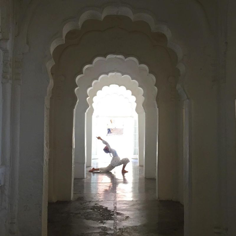 Ceci en una postura de yoga al fondo de un pasillo de arcos blancos