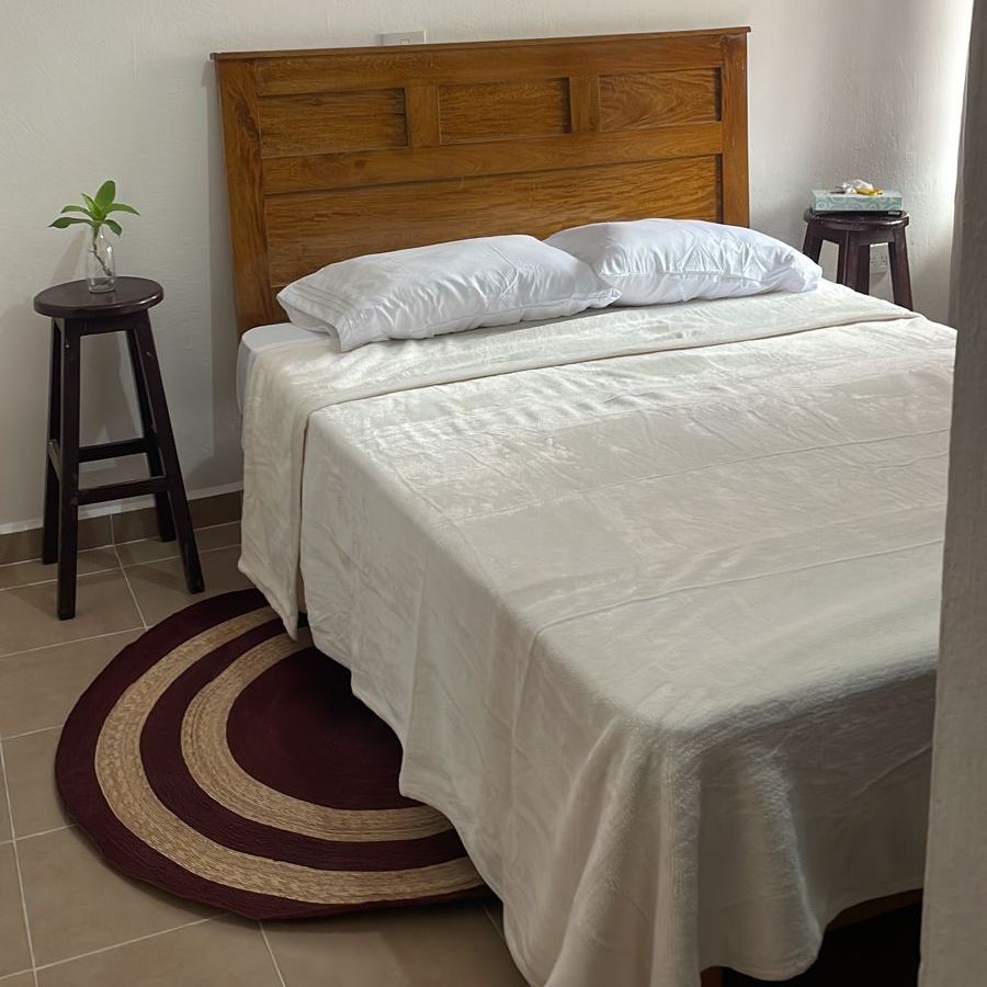 Recámara de la Yogui Suite con cama de cabecera de madera, ropa de cama blanca y tapete redondo